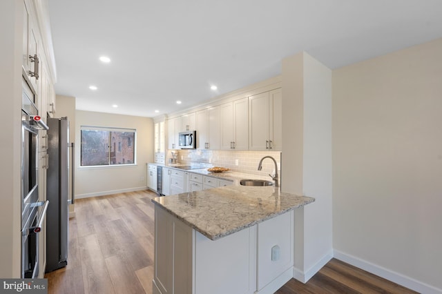 kitchen with sink, light stone counters, tasteful backsplash, white cabinets, and kitchen peninsula