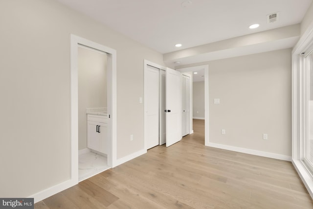 unfurnished bedroom with ensuite bathroom and light wood-type flooring