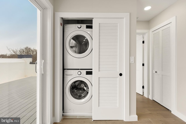 clothes washing area with a healthy amount of sunlight, stacked washer / drying machine, and light hardwood / wood-style flooring