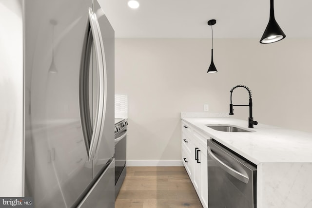 kitchen with sink, white cabinetry, hanging light fixtures, appliances with stainless steel finishes, and light hardwood / wood-style floors