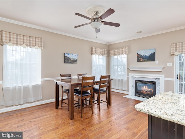 dining area with crown molding, ceiling fan, a fireplace, and light wood-type flooring