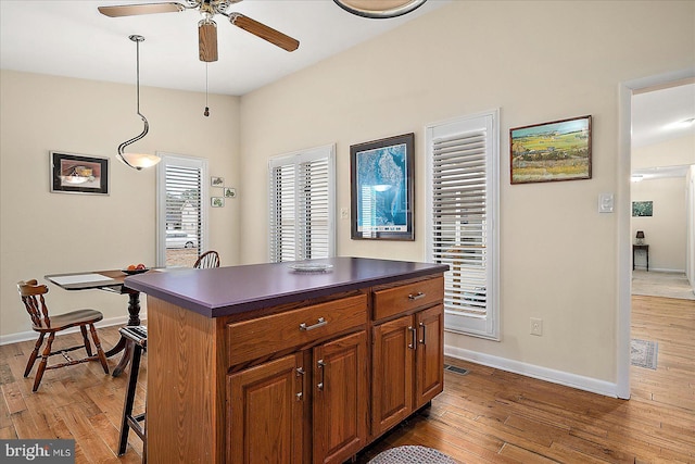 kitchen featuring wood-type flooring, decorative light fixtures, a center island, a kitchen breakfast bar, and ceiling fan