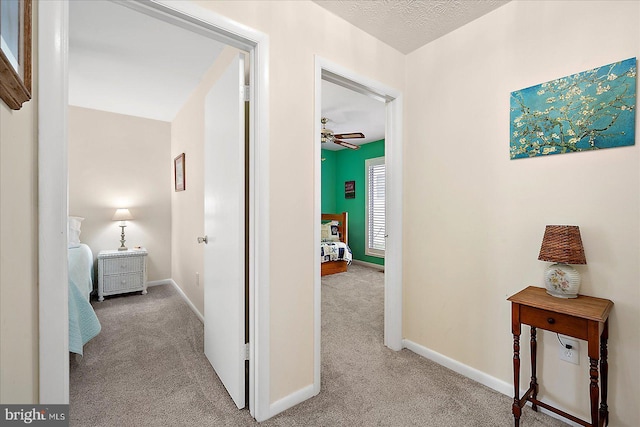 hall with light colored carpet and a textured ceiling