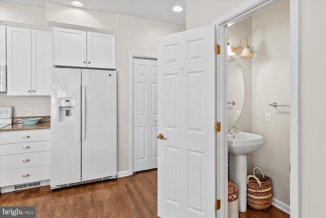 kitchen featuring white fridge with ice dispenser, dark stone countertops, white cabinets, and dark wood-type flooring