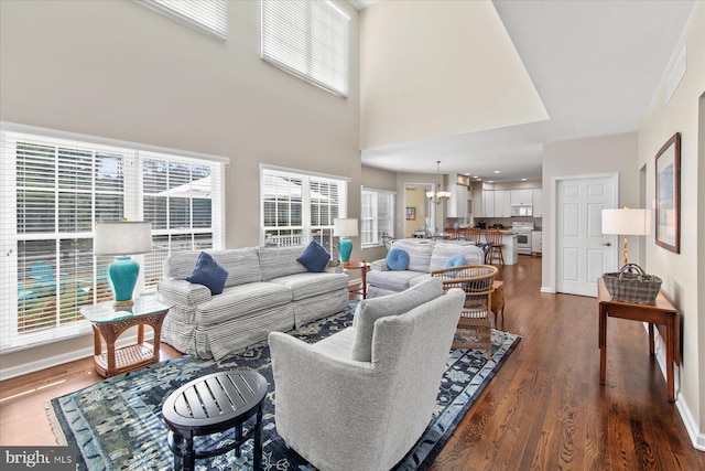 living room with a high ceiling, dark wood-type flooring, and an inviting chandelier