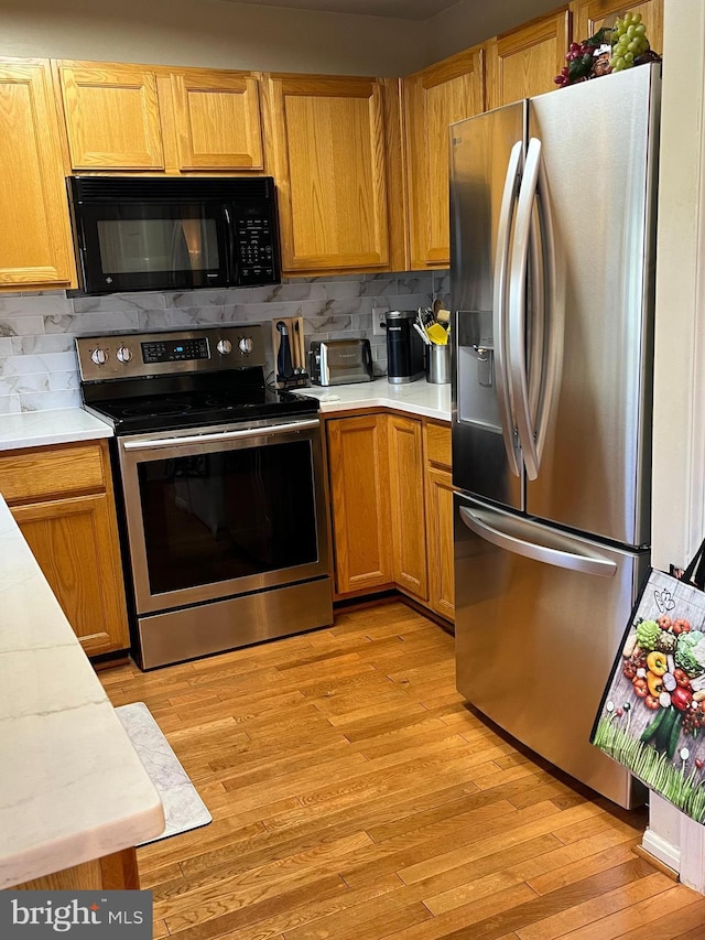 kitchen with appliances with stainless steel finishes, backsplash, and light hardwood / wood-style floors