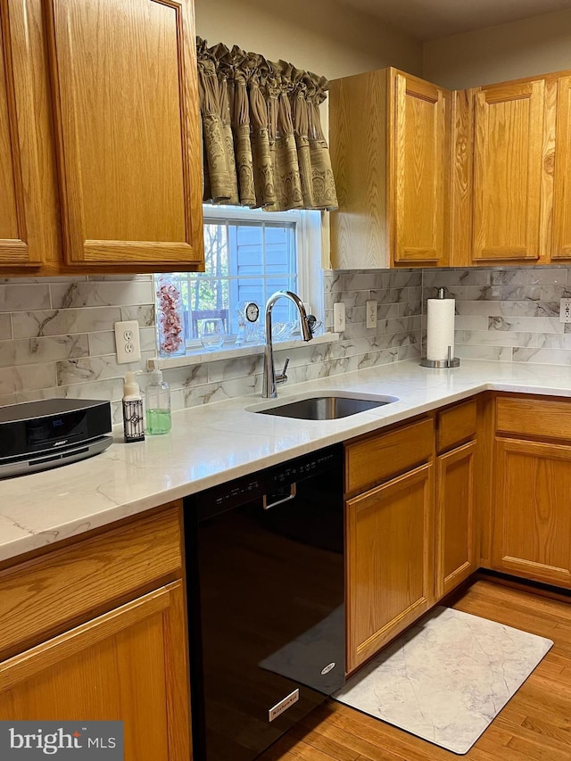 kitchen featuring sink, black dishwasher, light stone counters, tasteful backsplash, and light wood-type flooring