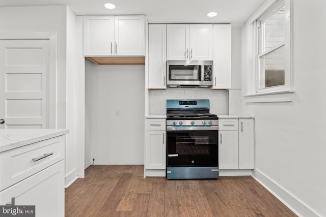 kitchen with appliances with stainless steel finishes, light stone counters, tasteful backsplash, white cabinets, and dark hardwood / wood-style flooring