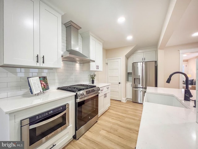 kitchen featuring wall chimney exhaust hood, sink, tasteful backsplash, stainless steel appliances, and white cabinets