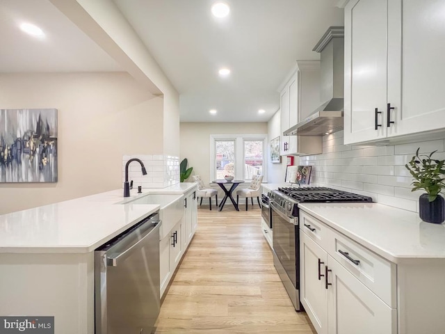 kitchen featuring wall chimney range hood, stainless steel appliances, sink, and white cabinets