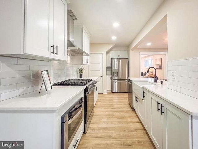 kitchen featuring sink, white cabinetry, stainless steel appliances, light hardwood / wood-style floors, and wall chimney exhaust hood