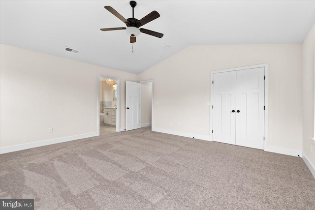 unfurnished bedroom featuring vaulted ceiling, light carpet, ensuite bath, and a closet