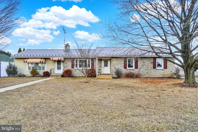 ranch-style home with entry steps, stone siding, a chimney, metal roof, and a front lawn