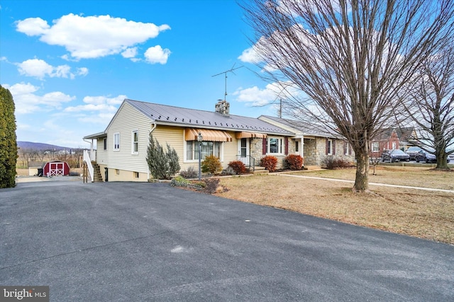 ranch-style house with a chimney, metal roof, stone siding, driveway, and stairs