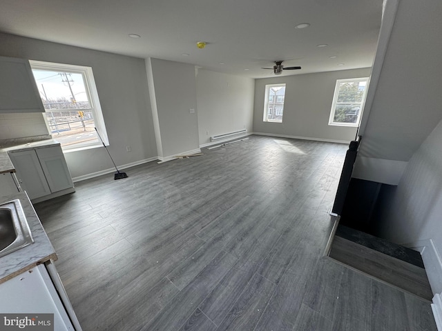 unfurnished living room with ceiling fan, wood-type flooring, sink, and a baseboard heating unit