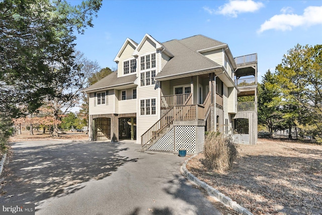 coastal home featuring a balcony, stairs, aphalt driveway, and roof with shingles