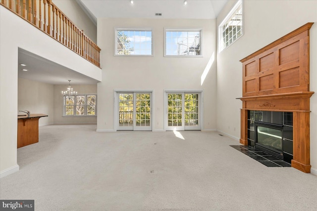 living room featuring baseboards, a tiled fireplace, a towering ceiling, carpet, and a notable chandelier