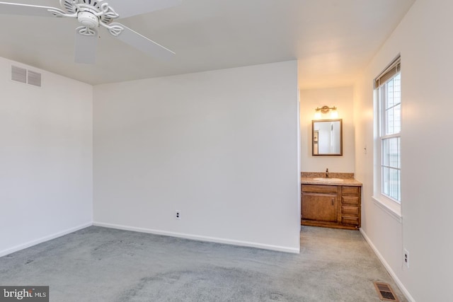 unfurnished bedroom featuring sink, light colored carpet, ceiling fan, and ensuite bathroom