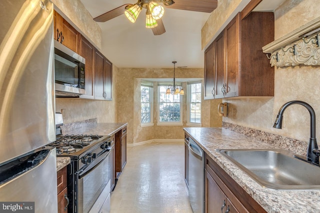 kitchen featuring appliances with stainless steel finishes, ceiling fan with notable chandelier, pendant lighting, sink, and light stone countertops