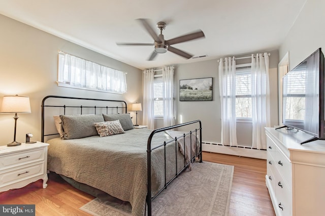 bedroom with baseboard heating, ceiling fan, and light hardwood / wood-style flooring