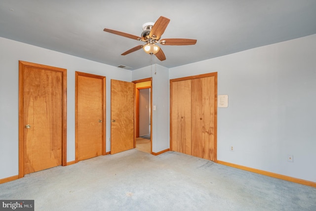 unfurnished bedroom featuring two closets, light colored carpet, and ceiling fan