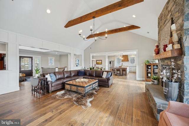 living room with beam ceiling, an inviting chandelier, a stone fireplace, high vaulted ceiling, and hardwood / wood-style flooring