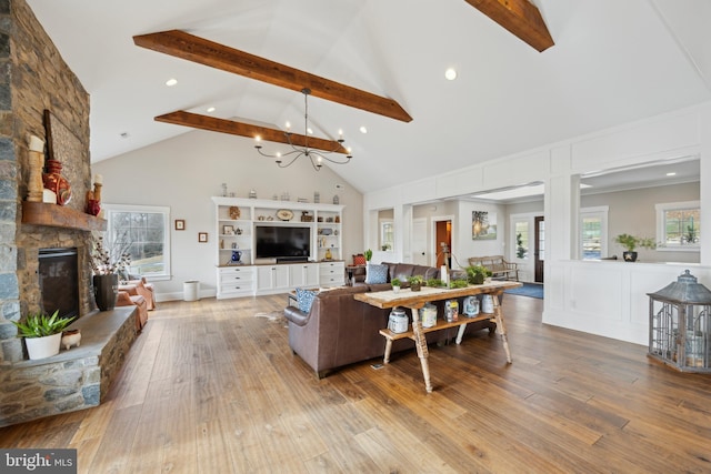 living area featuring a stone fireplace, beam ceiling, hardwood / wood-style floors, and a notable chandelier