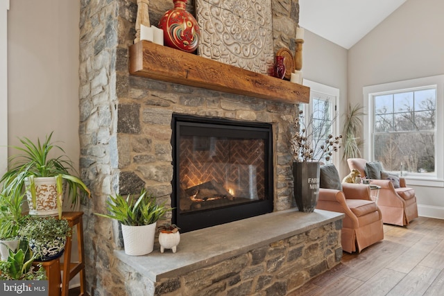 living area featuring lofted ceiling, baseboards, wood finished floors, and a stone fireplace