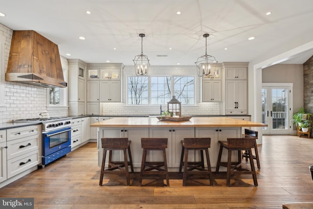 kitchen featuring a breakfast bar area, wood finished floors, a kitchen island, high end stainless steel range oven, and custom exhaust hood