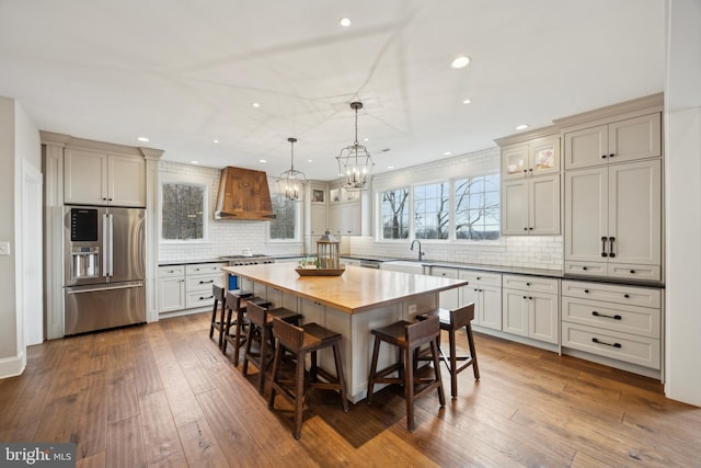 kitchen with dark wood-style flooring, a sink, high quality appliances, premium range hood, and a kitchen breakfast bar