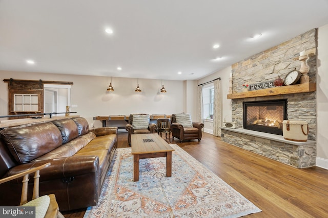 living area featuring a stone fireplace, a barn door, wood finished floors, and recessed lighting