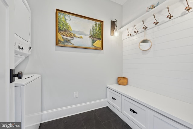 mudroom featuring dark tile patterned floors, stacked washer / dryer, and baseboards