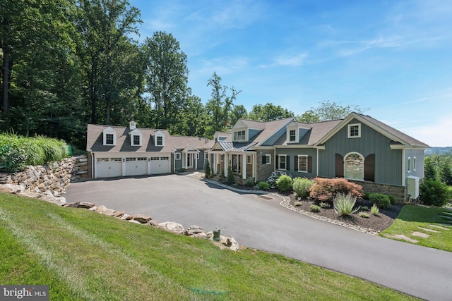 view of front of home featuring an attached garage, board and batten siding, a front yard, stone siding, and driveway