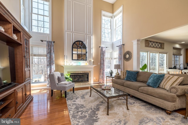 living room with a glass covered fireplace, plenty of natural light, wood finished floors, and ornate columns