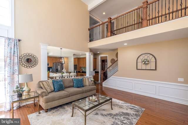 living room with a wainscoted wall, stairs, wood finished floors, a decorative wall, and ornate columns