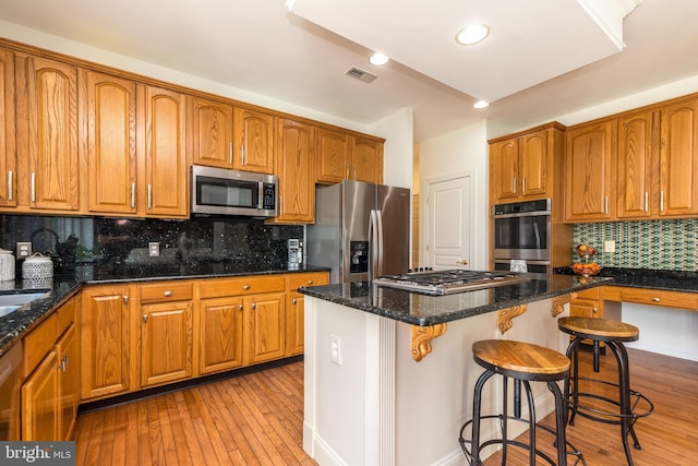 kitchen featuring visible vents, brown cabinets, a center island, stainless steel appliances, and light wood-style floors