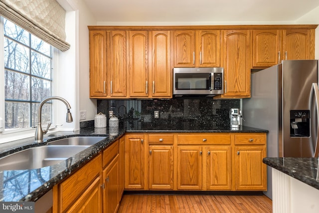 kitchen featuring tasteful backsplash, dark stone counters, brown cabinetry, stainless steel appliances, and a sink