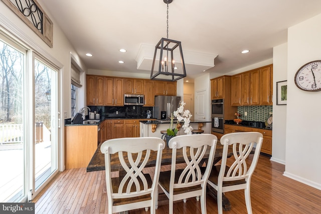 kitchen with light wood finished floors, a sink, appliances with stainless steel finishes, dark countertops, and a center island