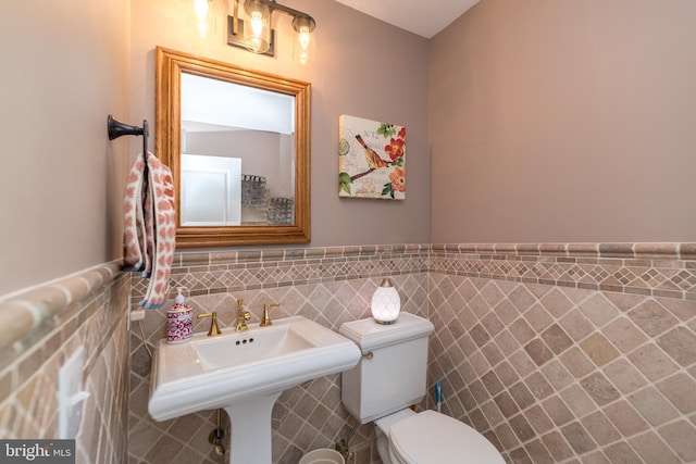 bathroom with a wainscoted wall, toilet, tile walls, and a sink