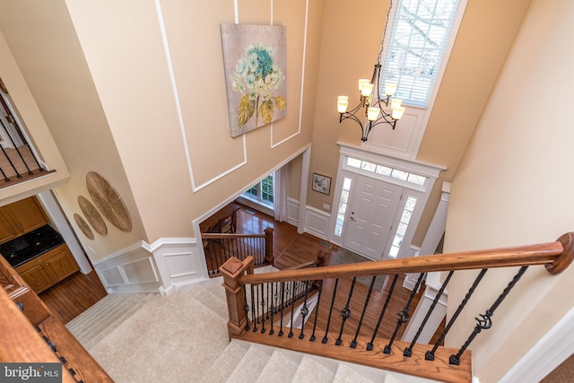 entryway featuring stairs, a decorative wall, a towering ceiling, and a chandelier