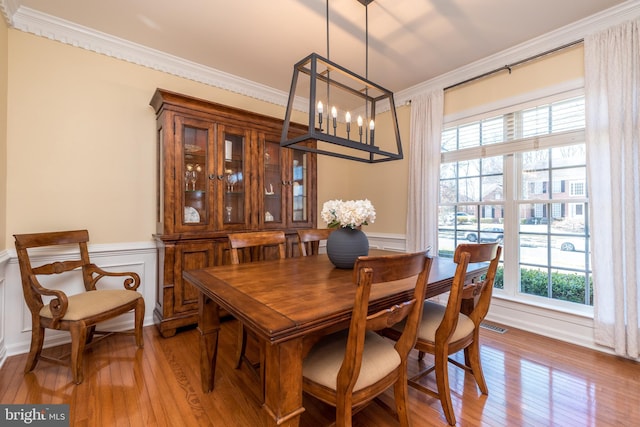 dining space with light wood-style flooring, a decorative wall, wainscoting, and ornamental molding