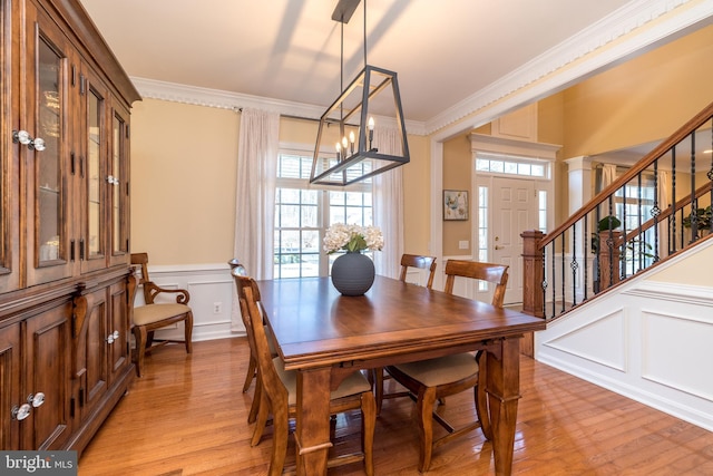 dining area with light wood-style floors, ornamental molding, stairs, and a decorative wall