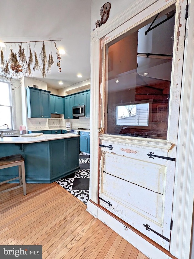 kitchen featuring stainless steel microwave, a breakfast bar area, blue cabinets, light countertops, and light wood-style floors