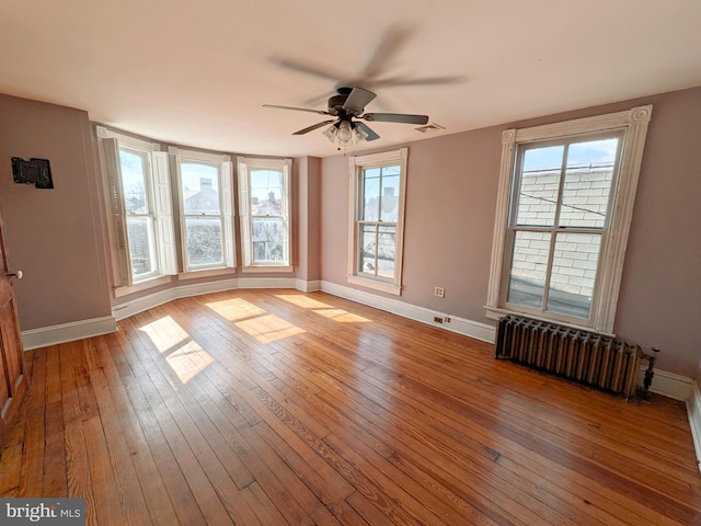 unfurnished room with radiator, light wood finished floors, baseboards, and visible vents