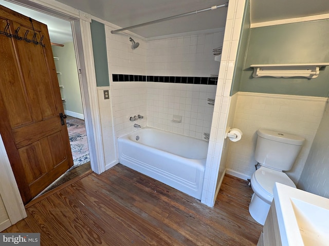 bathroom featuring a wainscoted wall, tile walls, toilet, tub / shower combination, and wood finished floors