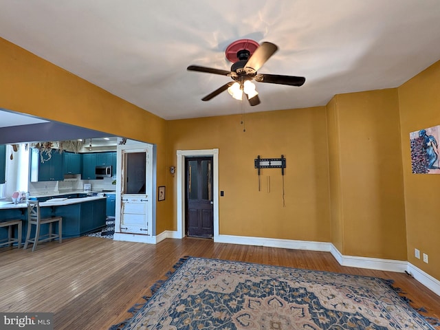 interior space with wood finished floors, a ceiling fan, and baseboards