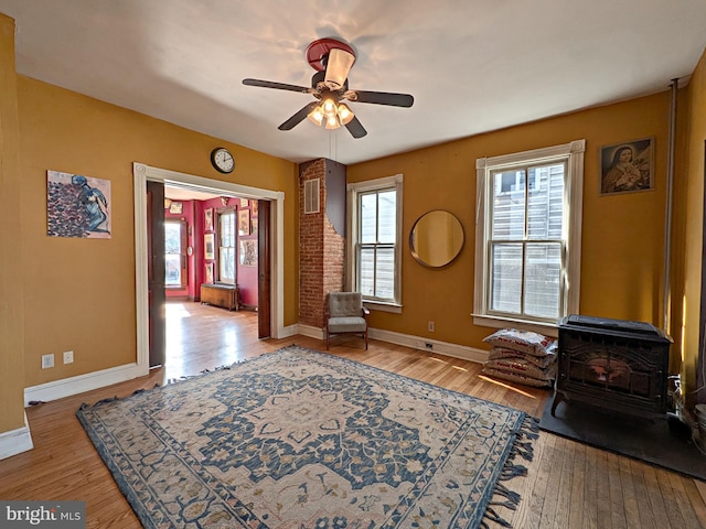 living area featuring plenty of natural light, wood finished floors, a wood stove, and baseboards