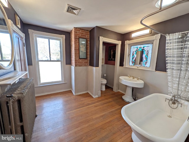 full bath with visible vents, a freestanding bath, toilet, radiator heating unit, and wood finished floors