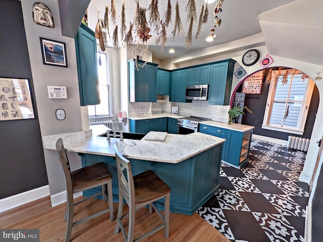 kitchen featuring a peninsula, stainless steel appliances, a sink, a kitchen breakfast bar, and blue cabinetry