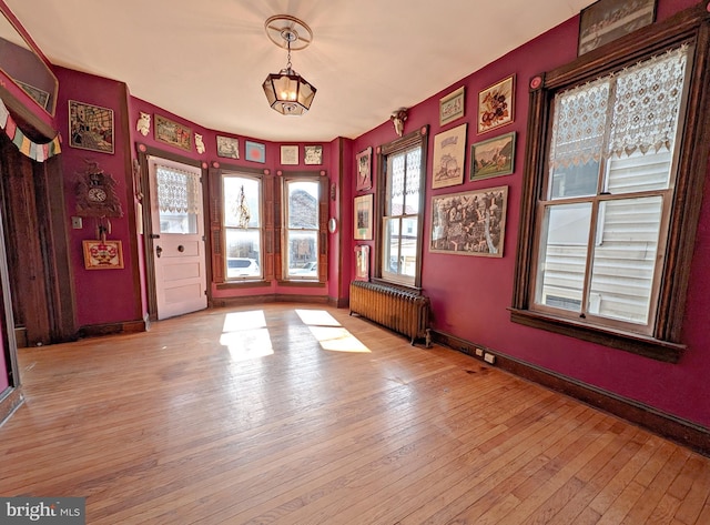 unfurnished room featuring radiator, light wood-style floors, and baseboards